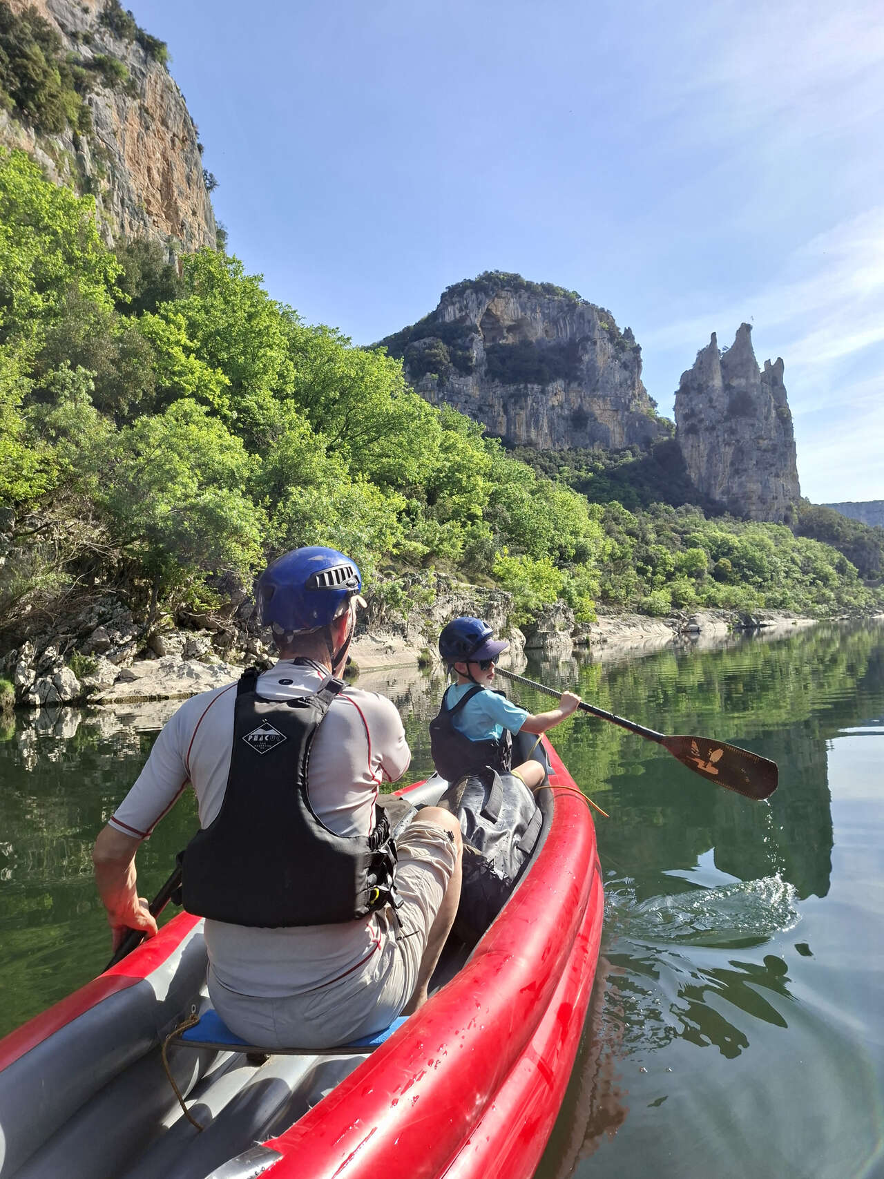 Canoë rouge glissant sur les eaux calmes face au rocher de la Cathédrale en Ardèche