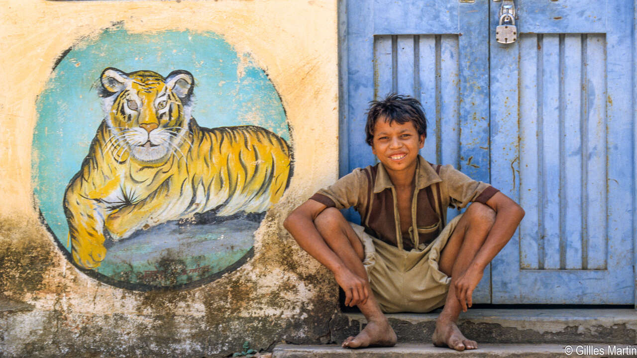 Enfant assis devant une fresque de tigre dans un village près de Bandhavgarh en Inde