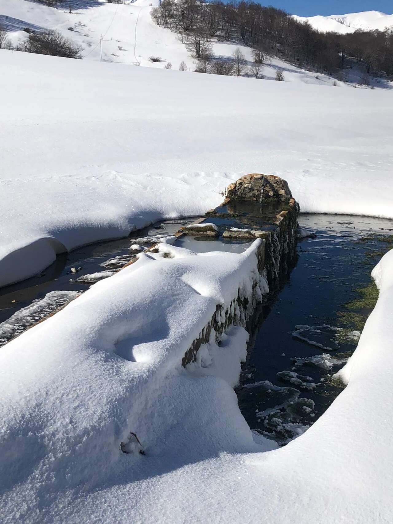 Fontaine en pierre entourée de neige dans les Abruzzes – contraste entre eau vive et paysage hivernal avec Amarok
