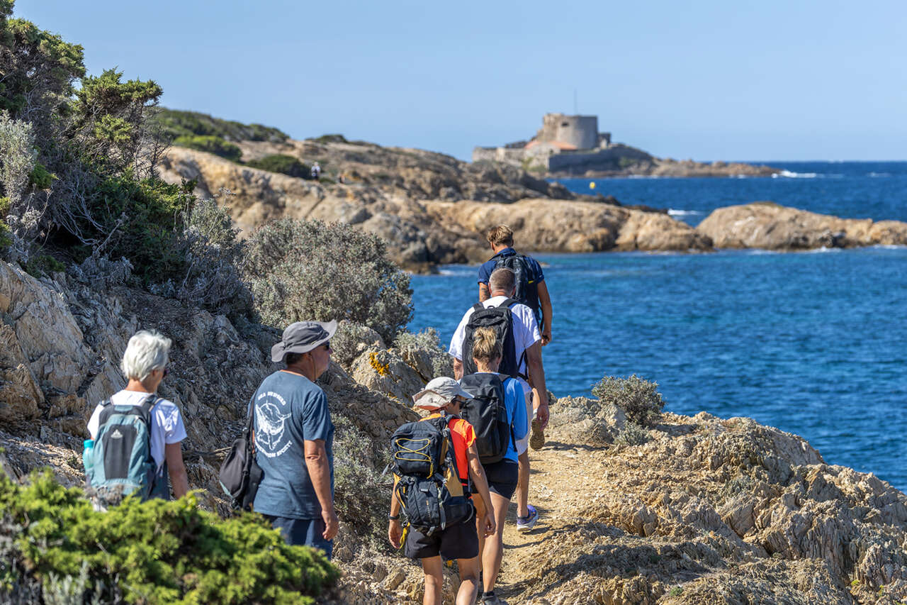 Groupe de randonneurs sur un sentier côtier rocheux dominant les eaux turquoise de Méditerranée